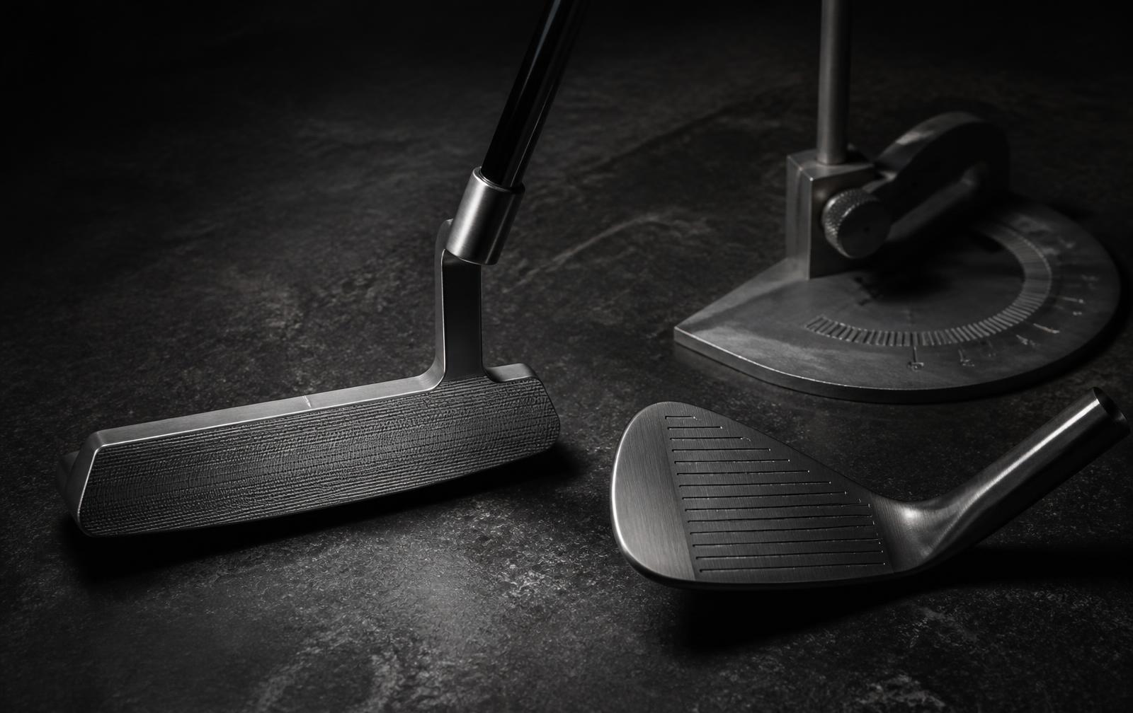 Putter, wedge and a loft and lie gauge on a dark workshop surface